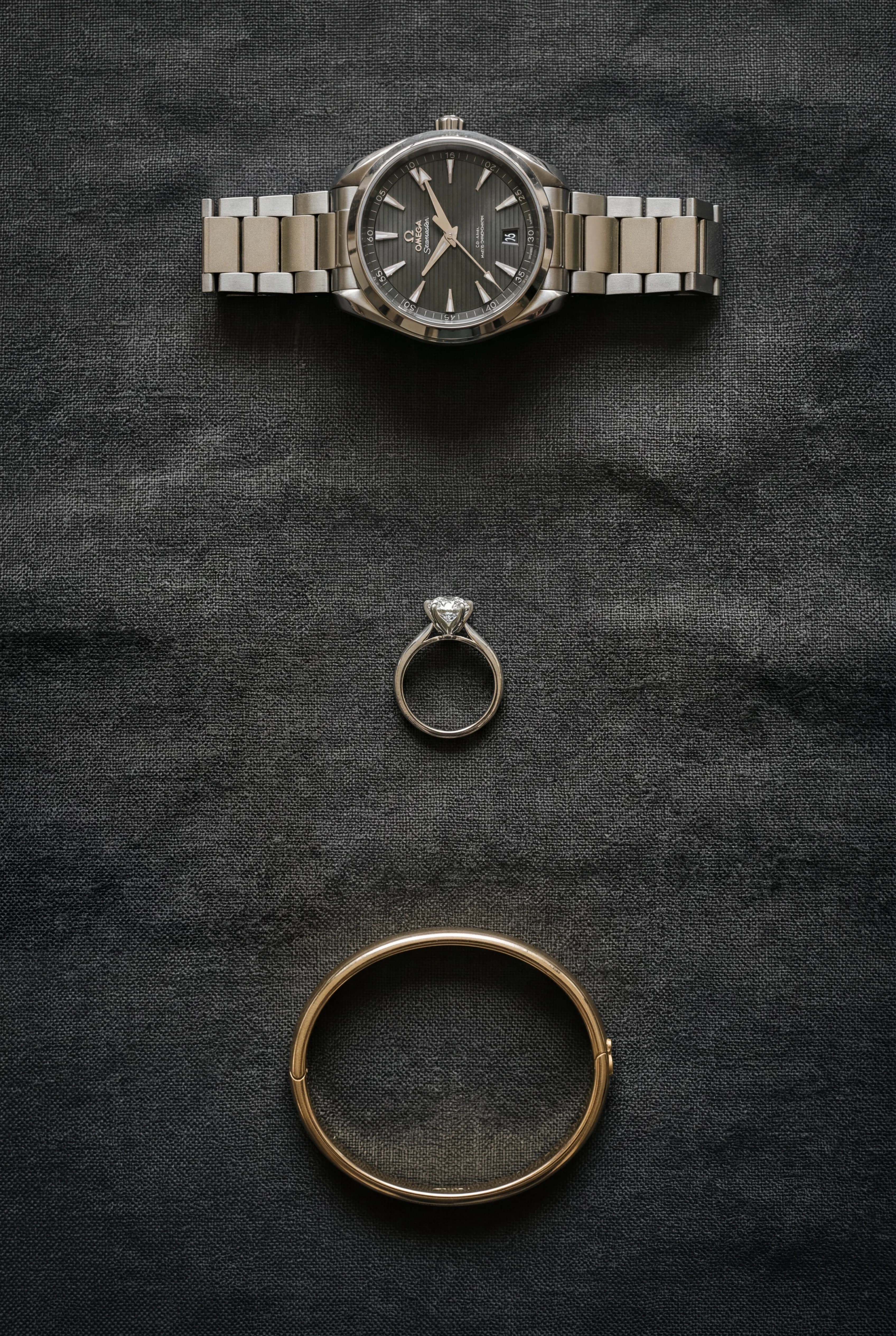 Luxury watch, ring and gold bangle arranged on a dark flat surface
